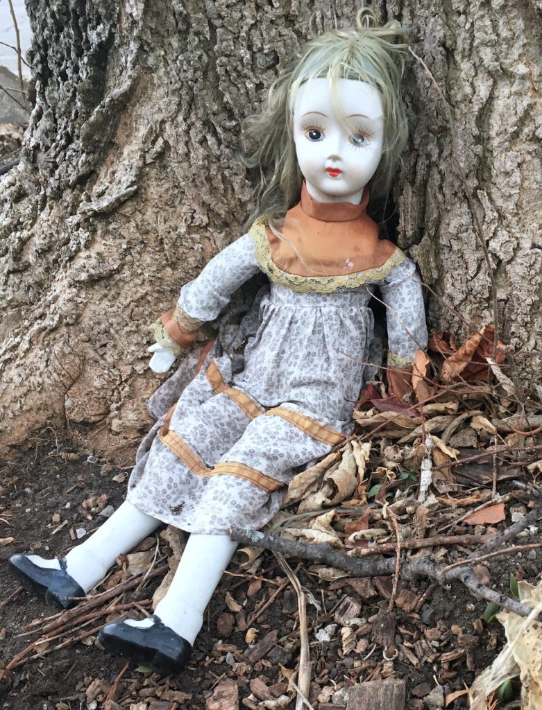 Doll sitting against a tree trunk